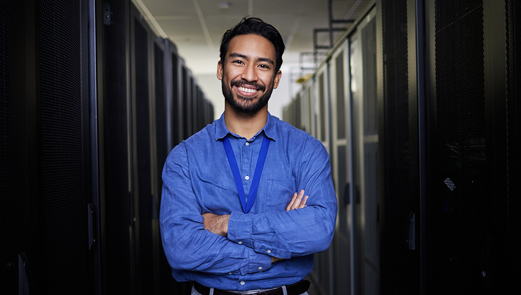 An IT outsourcing expert stands smiling in a server room, ready to help.