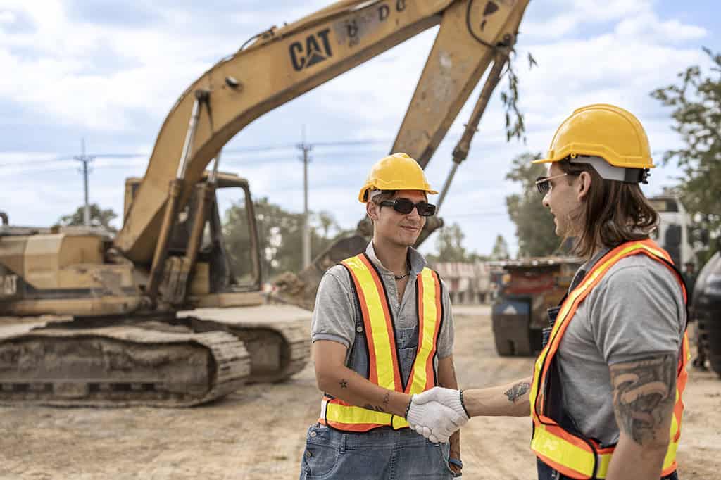 Construction company workers in hard hats and reflective vests shaking hands at a construction site