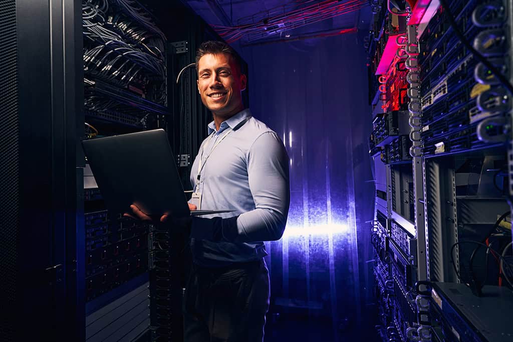 An IT expert stands smiling in a cloud server farm