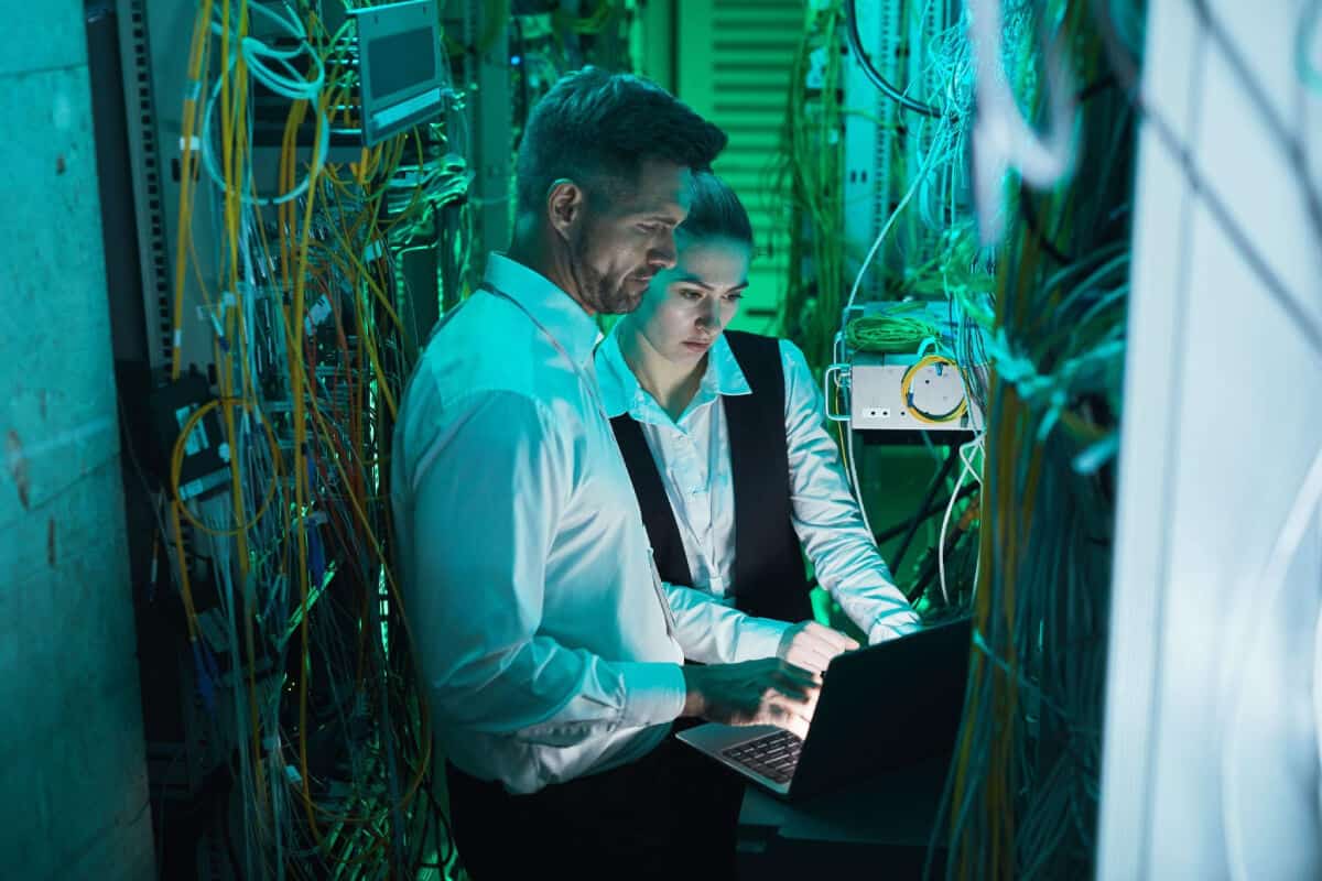 IT specialist working with member of in-house team in server room during cybersecurity incident