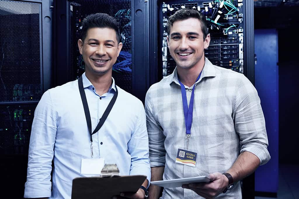 Smiling IT technicians standing in front of a server farm.