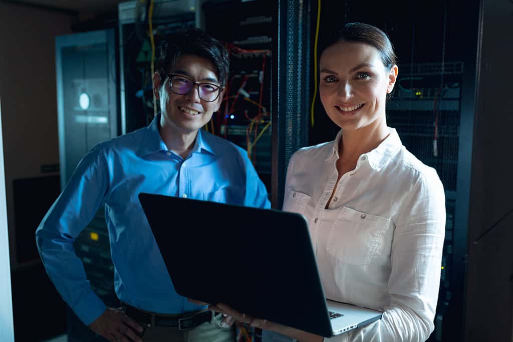 Two IT experts smiling by a server farm.