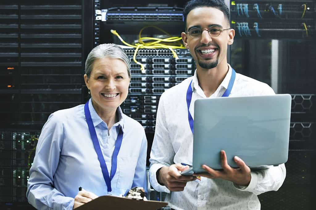 Two IT specialists in a server room stand smiling, ready to help.