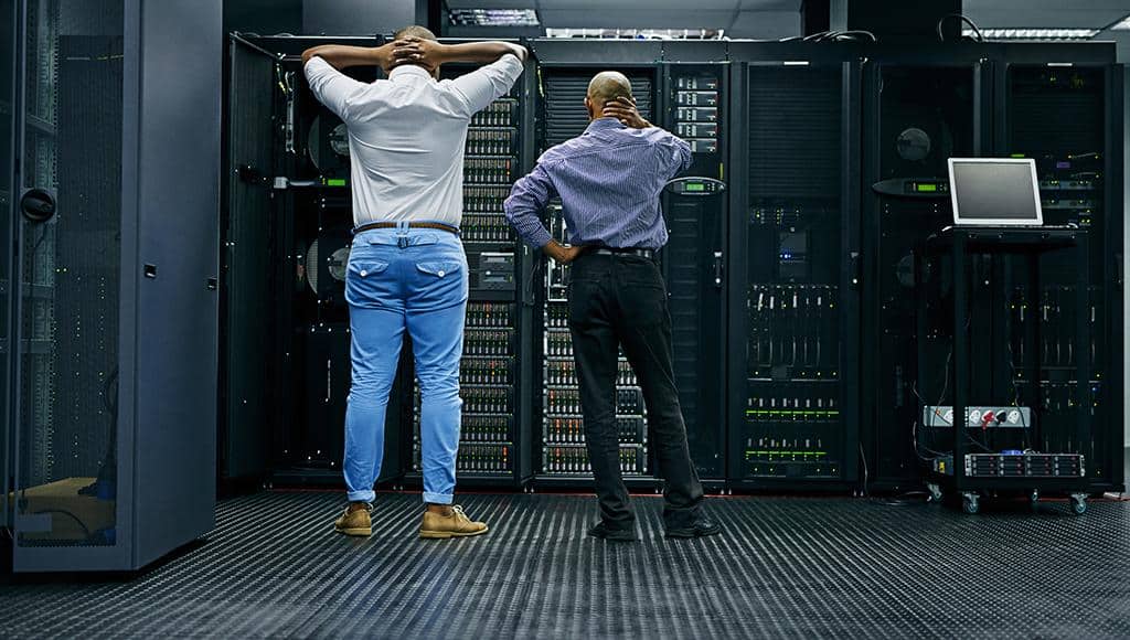 Two IT specialists stare at a server rack during a data loss crisis.