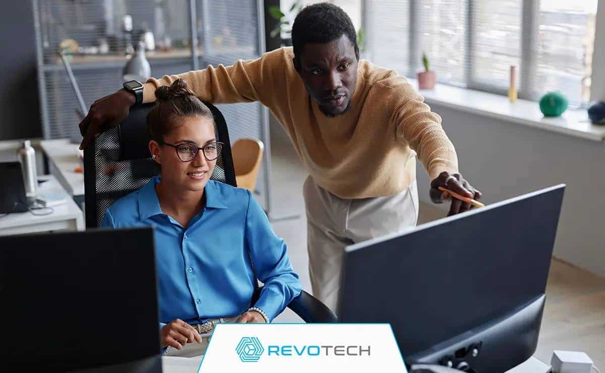 Two office colleagues at a desk looking at a computer monitor troubleshooting an IT issue.