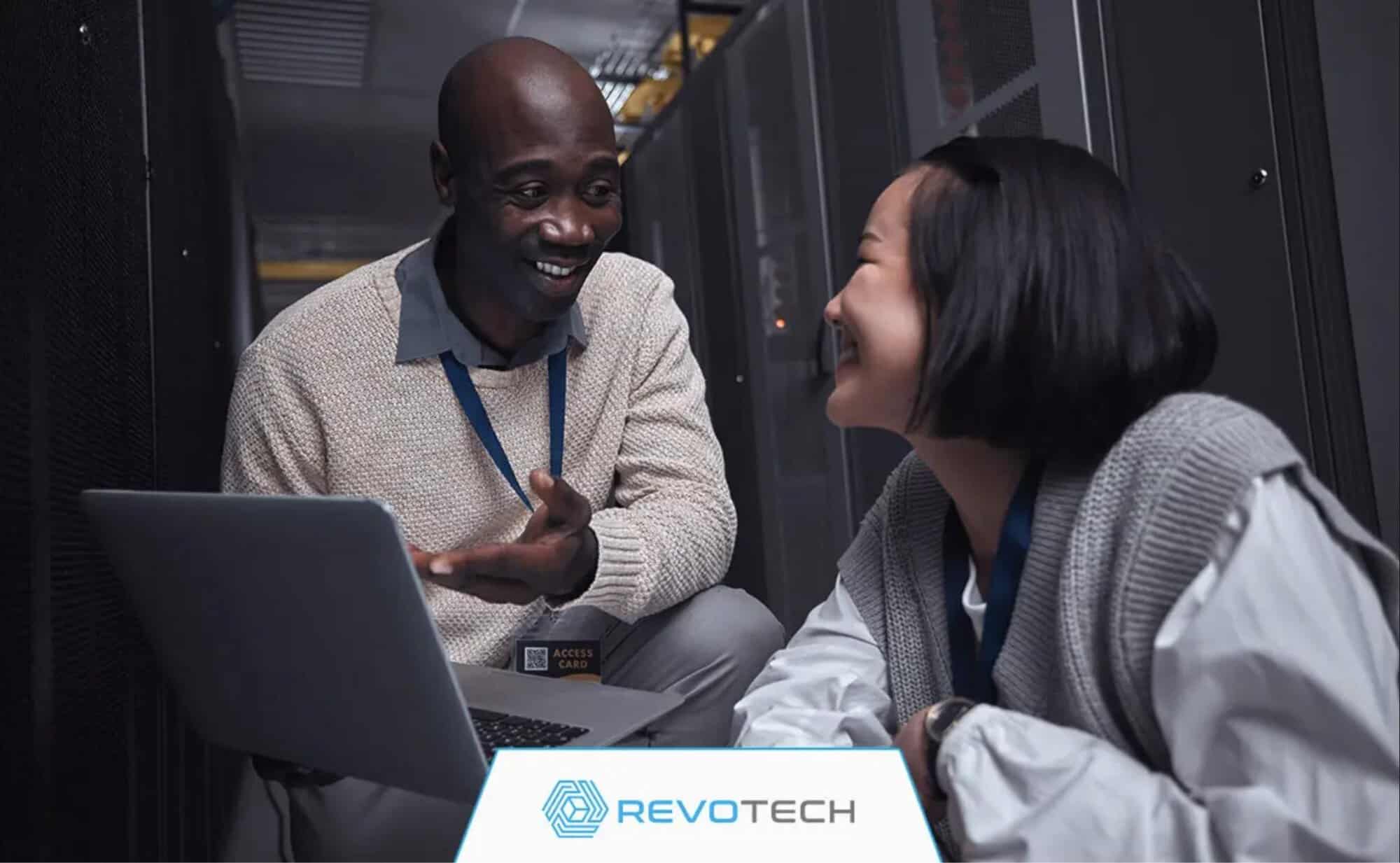  Two smiling IT professionals crouched by hardware and an open laptop discussing risk reduction.
